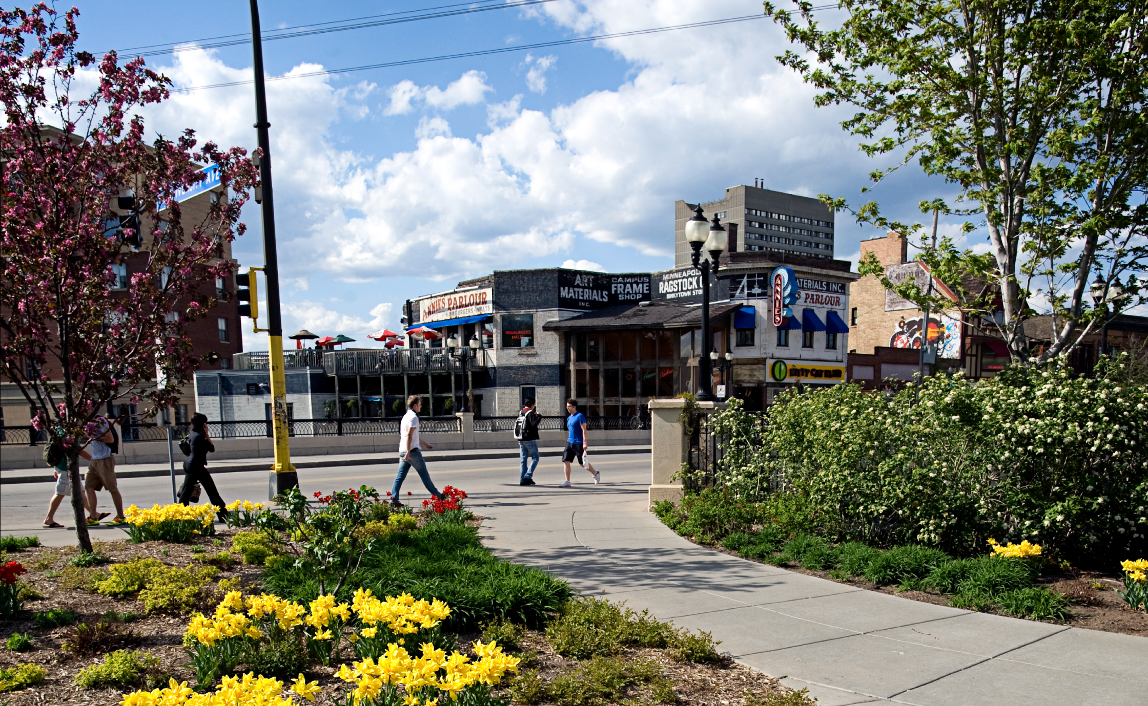 View through a campus garden of students walking in the Dinkytown business area.