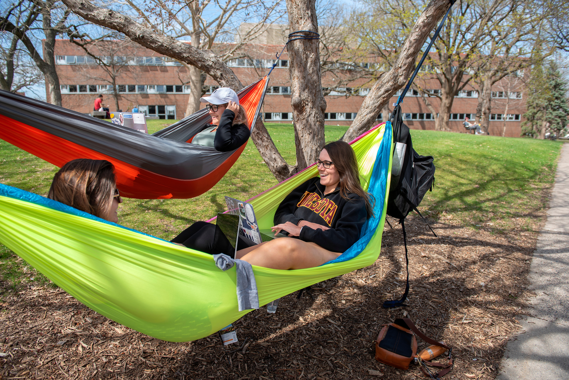 Three students hanging in two hammocks at the knoll.