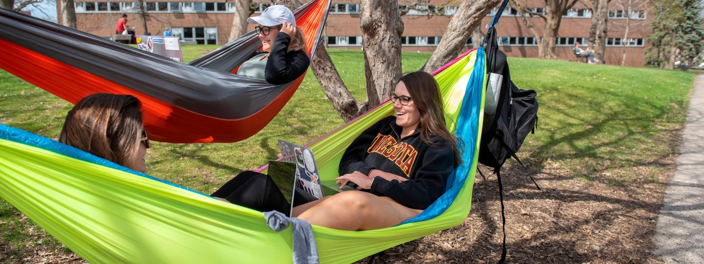 Three students hanging in two hammocks at the knoll.