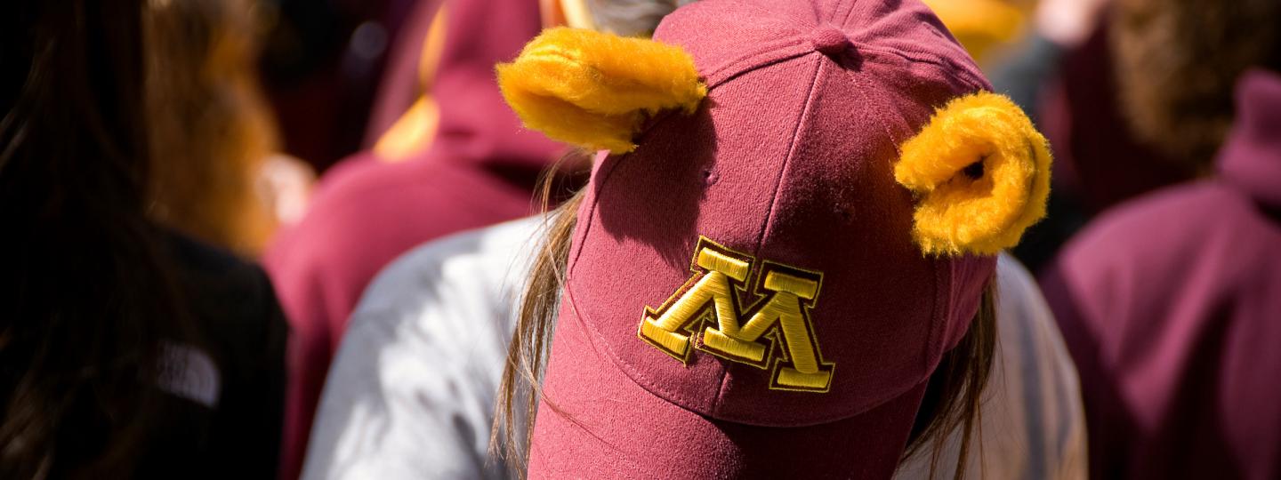 A person wearing a backward U of M hat with gopher ears on top