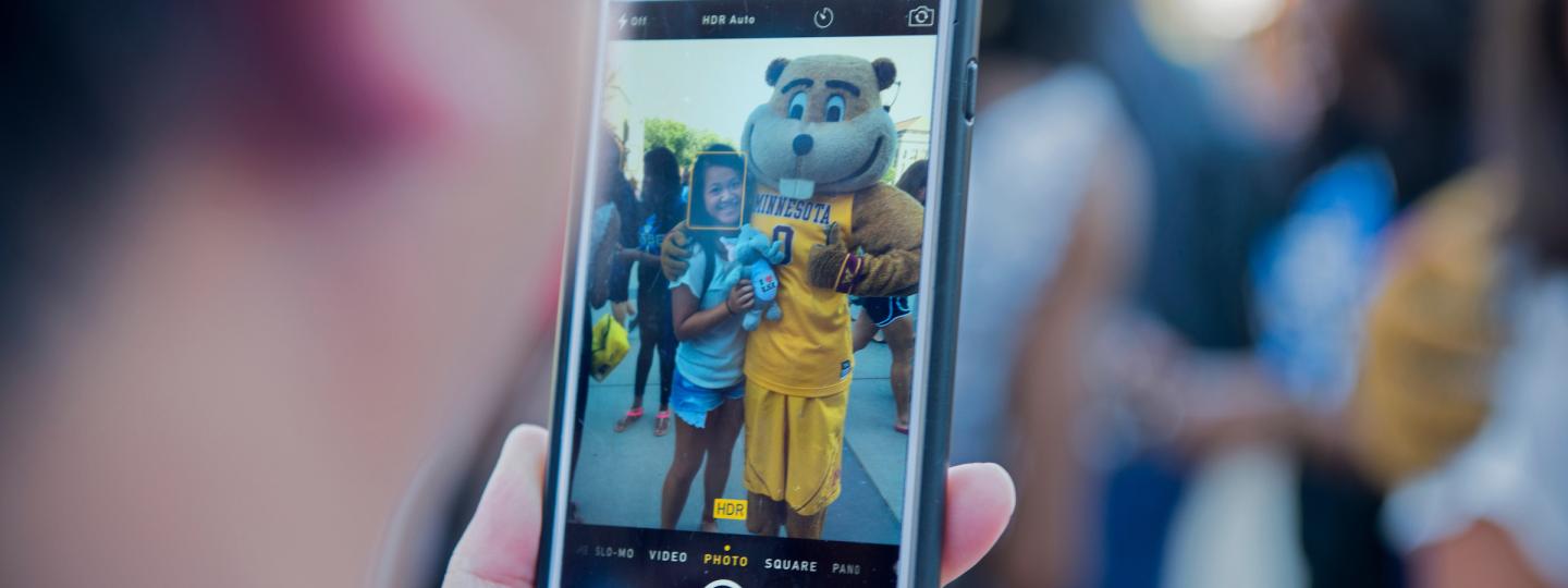 View of a cell phone taking a picture of a student with the Goldy mascot