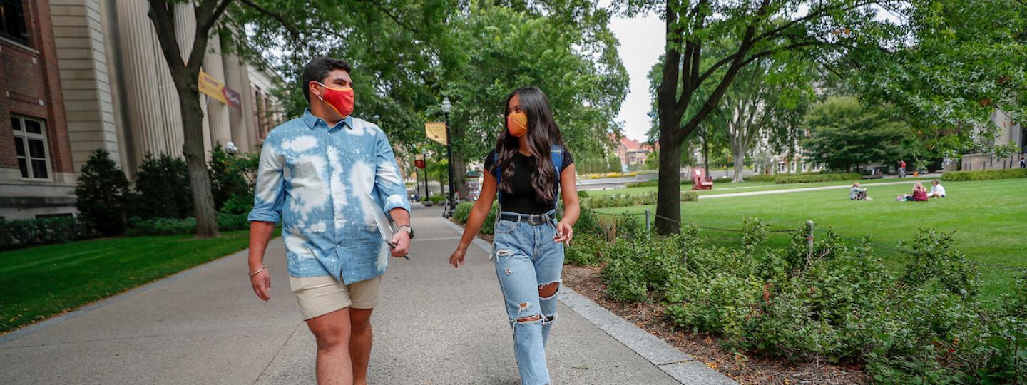 Two students wearing masks walk outside on campus