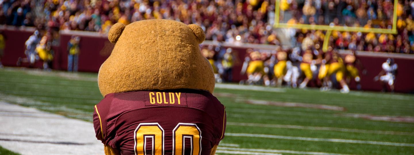 Goldy Gopher mascot sitting on the footbll field, facing away from the camera