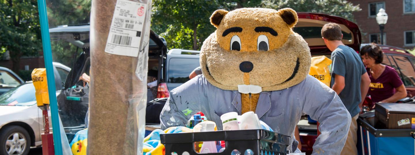 Goldy Gopher pushing a moving cart with a student's belongings