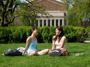 Two students sit in the grass on the mall on a warm day.