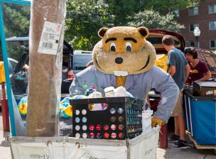 Goldy Gopher pushing a moving cart with a student's belongings