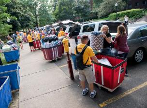 A row of cars parked in parking spots as students and helpers unload items into moving carts