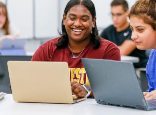 two people looking at their laptops and smiling