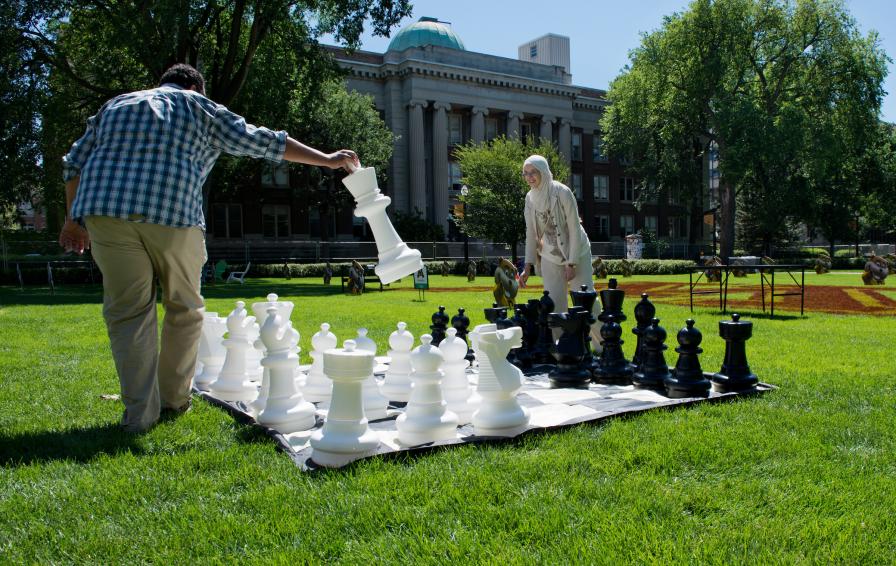 Students playing chess on an oversized board outside